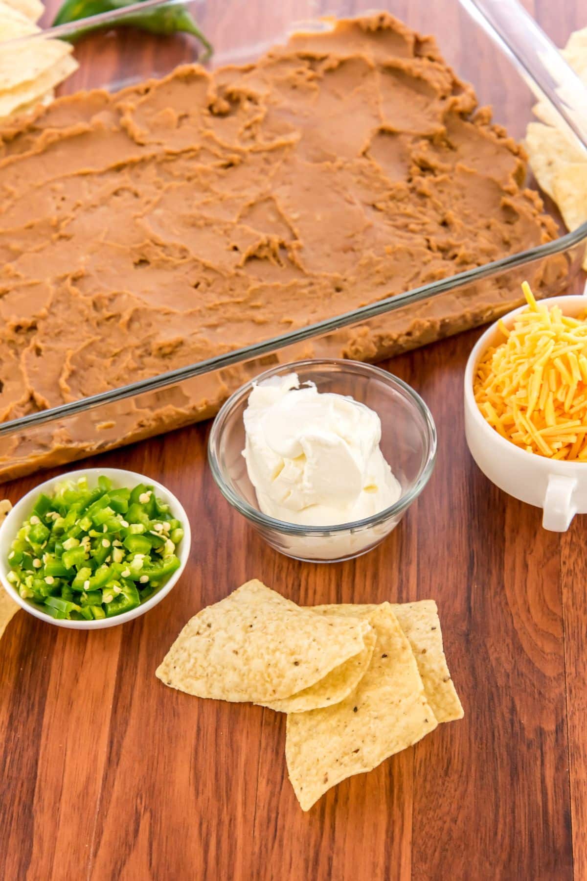 Bean dip in a glass pan next to bowls filled with other ingredients.