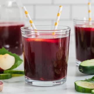 A glass of beet juice with two straws and a lemon slice.