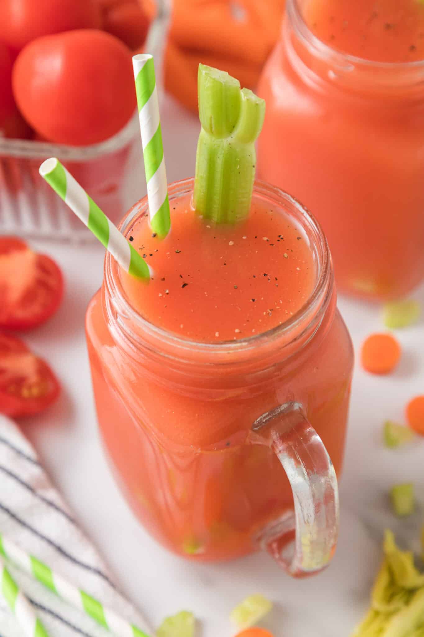 Large handled mason jar with tomato juice that has two straws and a celery stalk.