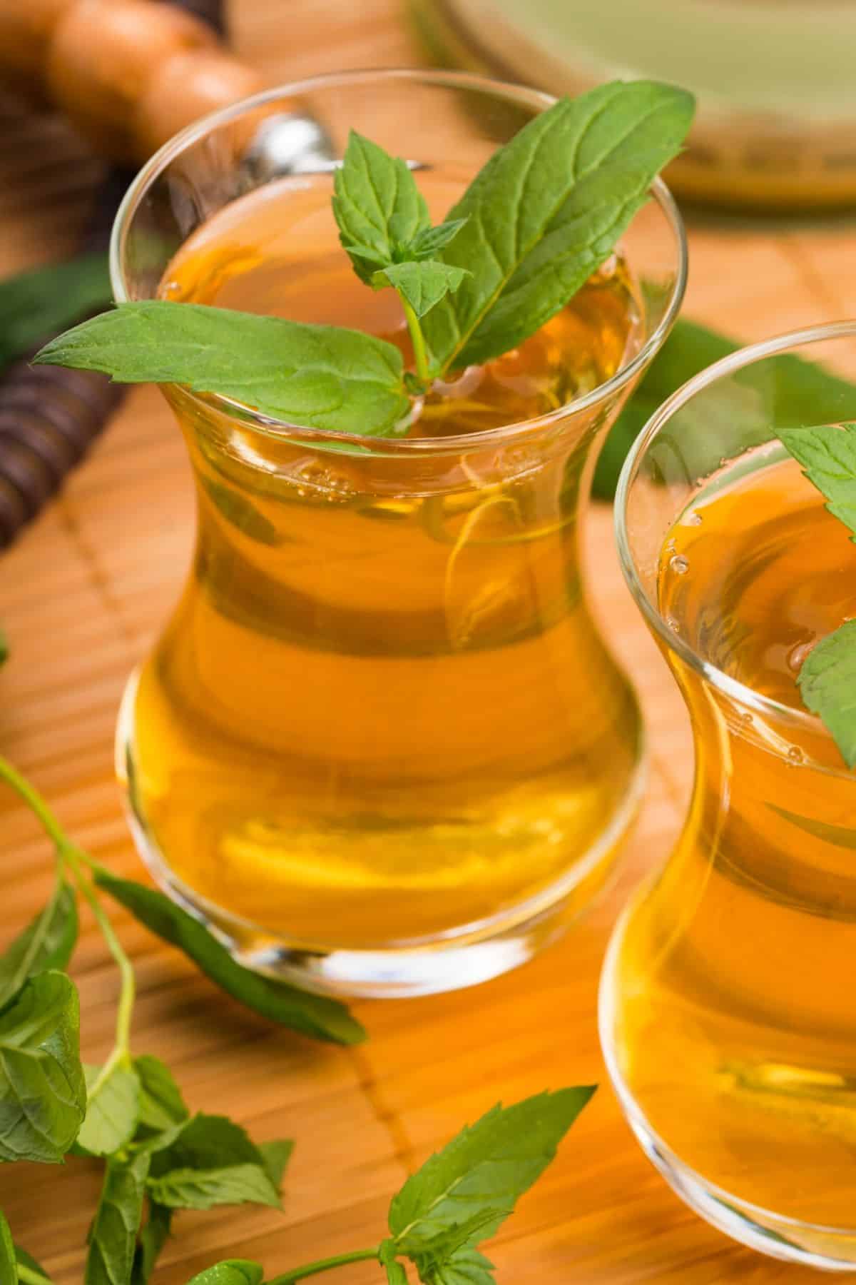 Two glasses filled with tea and mint leaves.
