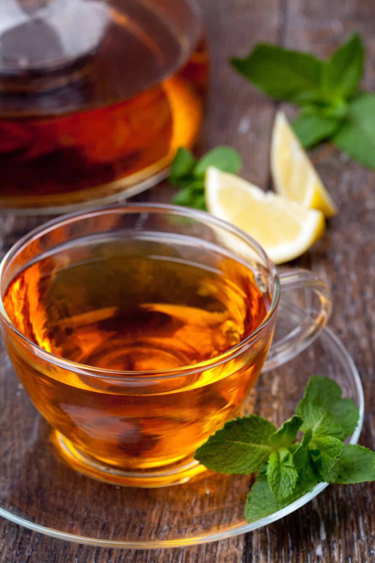 Glass tea cup filled with tea on a glass plate with mint garnish.