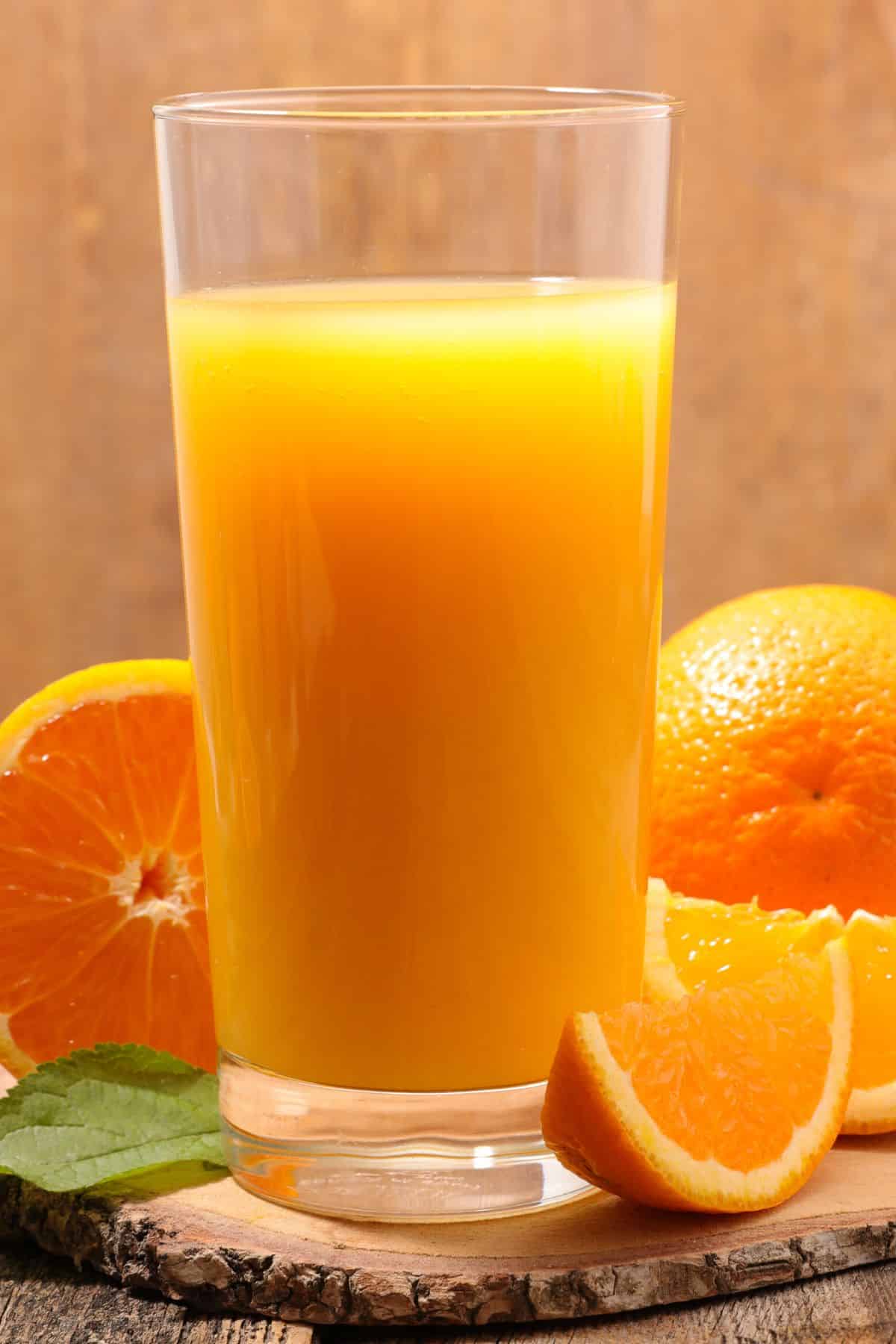 Tall glass filled with orange juice surrounded by orange slices.