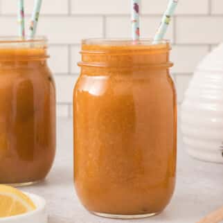 Two mason jars filled with peach juice and two straws each.