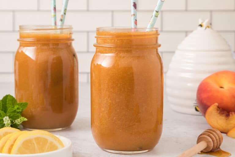 Two mason jars filled with peach juice and two straws each.