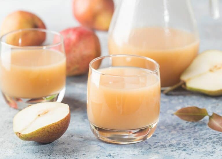 Two short glasses of pear juice next to a glass pitcher.