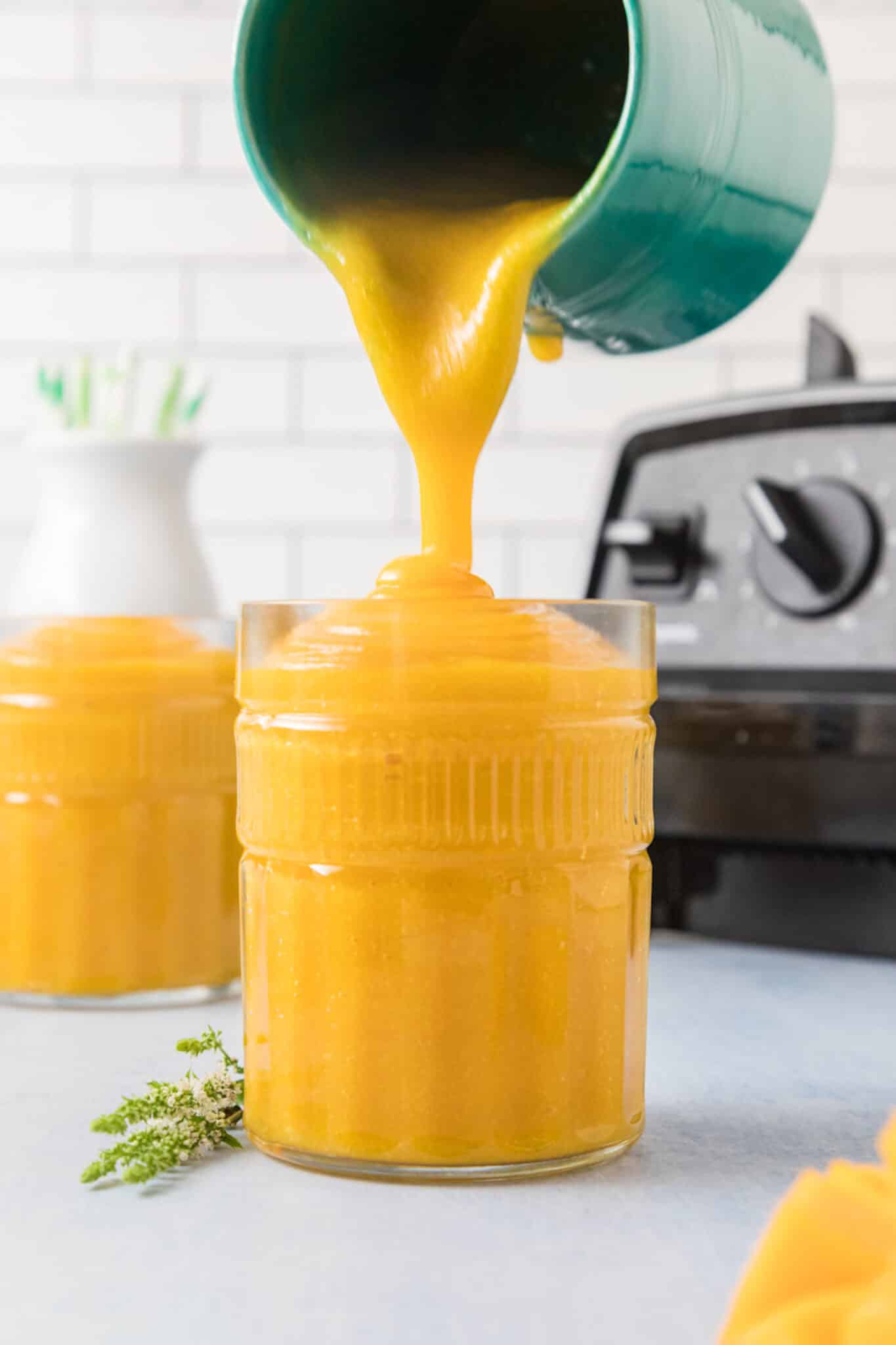 A turquoise pitcher pouring mango juice into a glass.