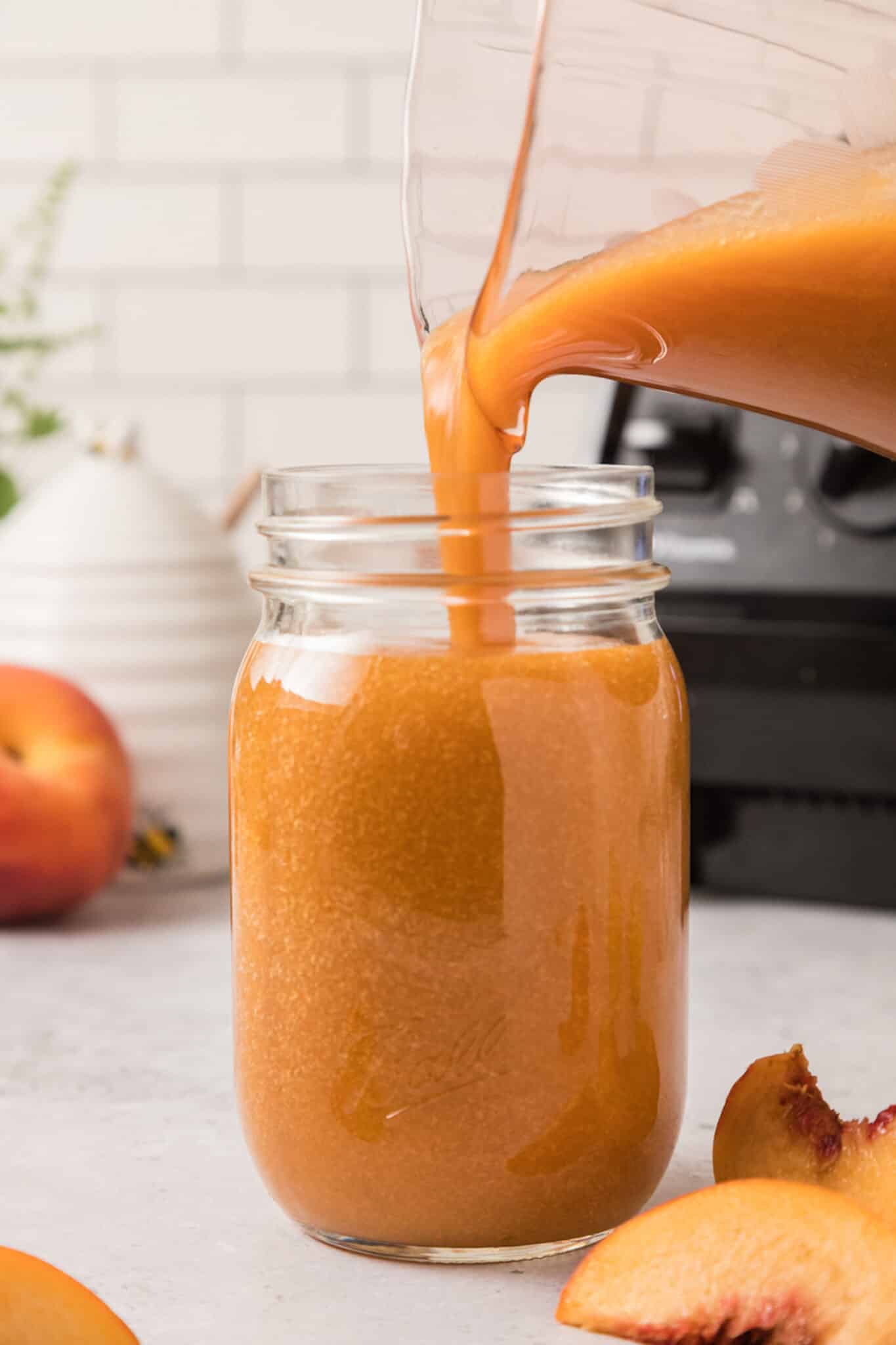 A glass pitcher pouring peach juice into a Mason jar.