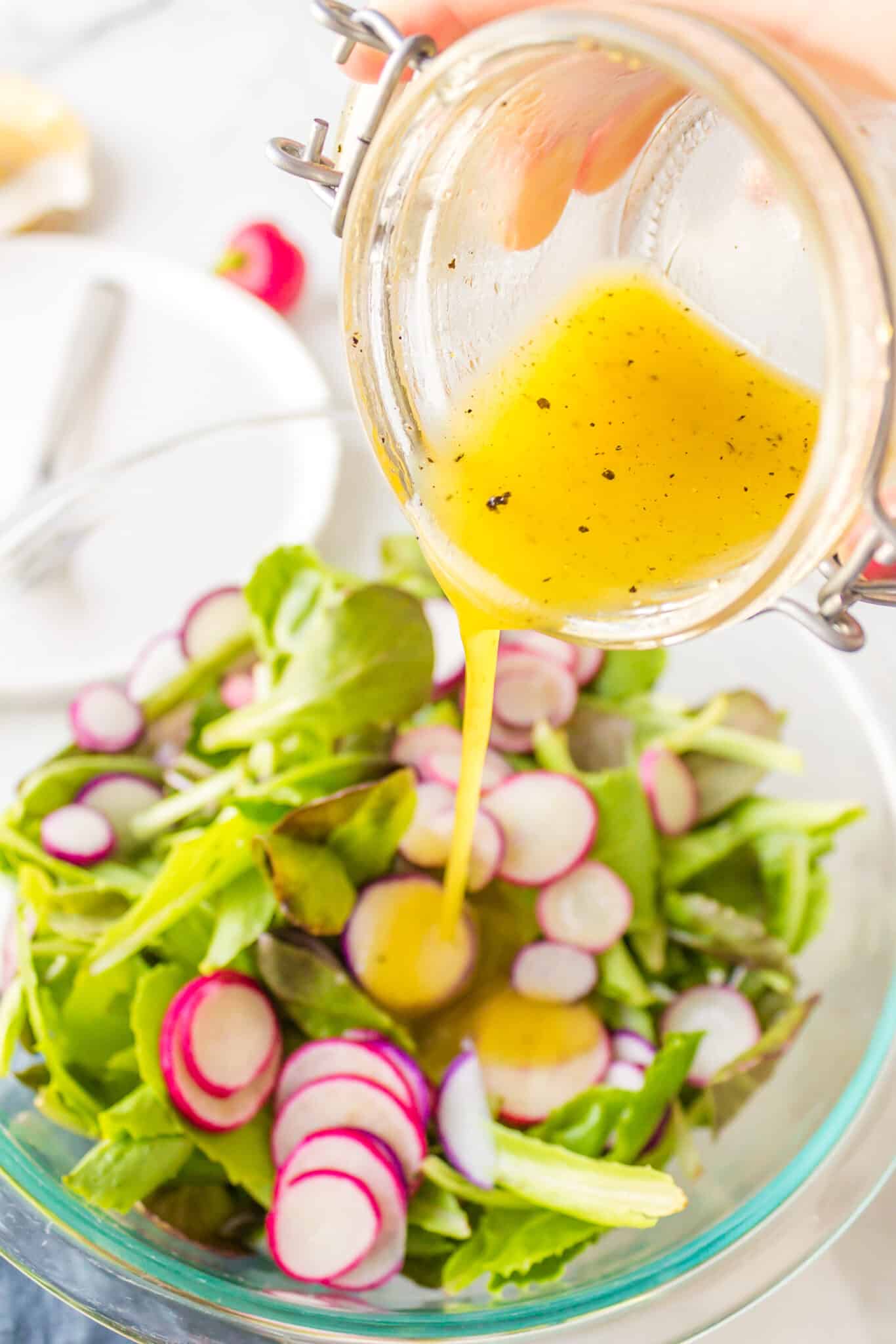 Pouring dressing from a jar onto a baby romaine salad.