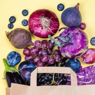 Many blue and purple fruits and veggies spilling out of a paper bag.