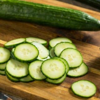Whole cucumbers and fresh sliced rounds on a wooden cutting board.