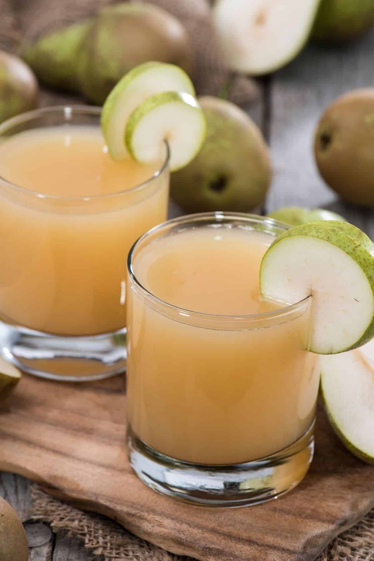 Two short glasses of pear juice with a pear wheel on the rim.