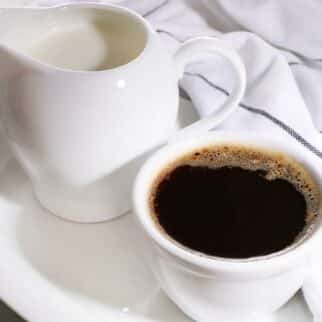 a mug of coffee beside a small pitcher of creamer.