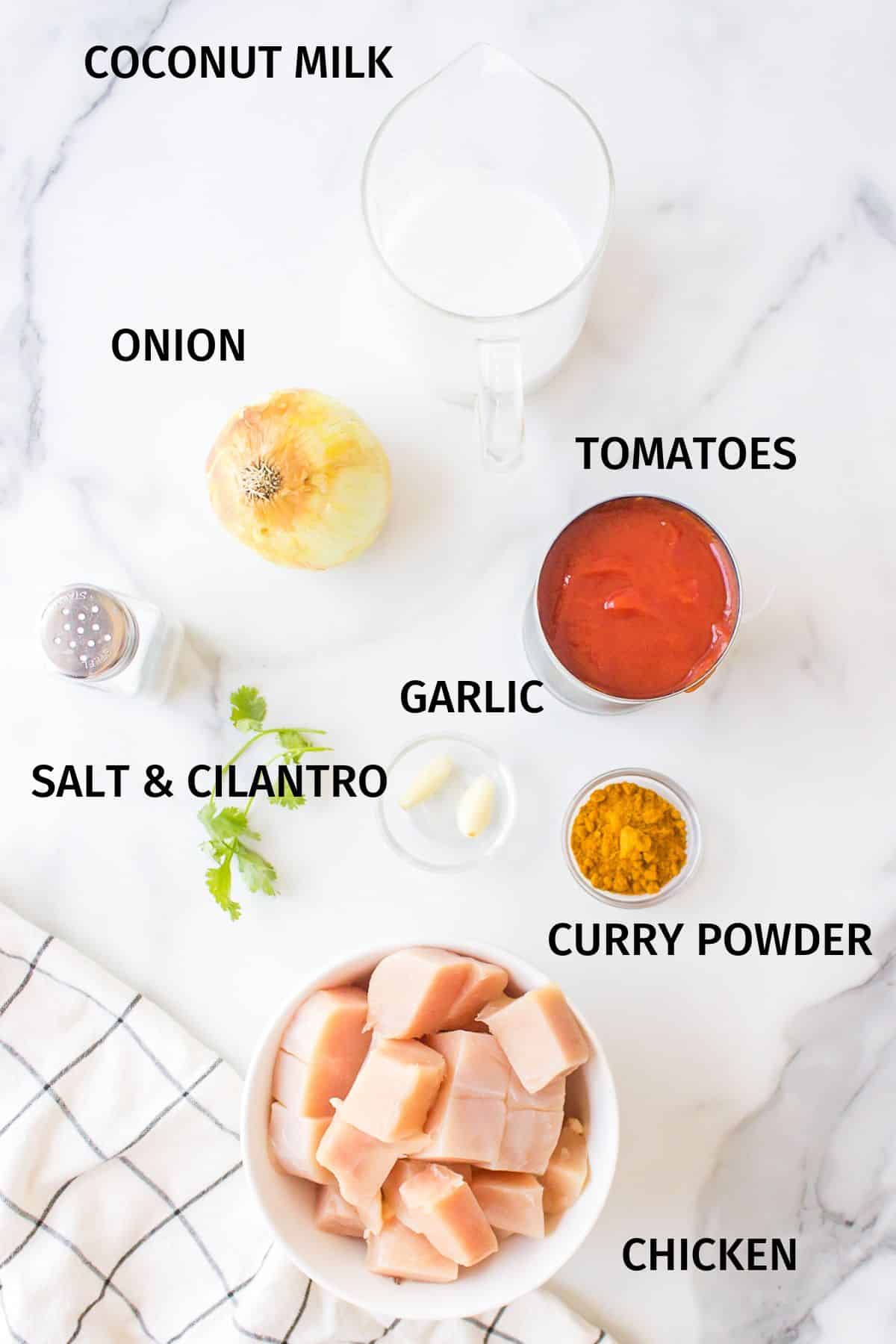 Ingredients to make simple chicken curry in small bowls on a white surface.