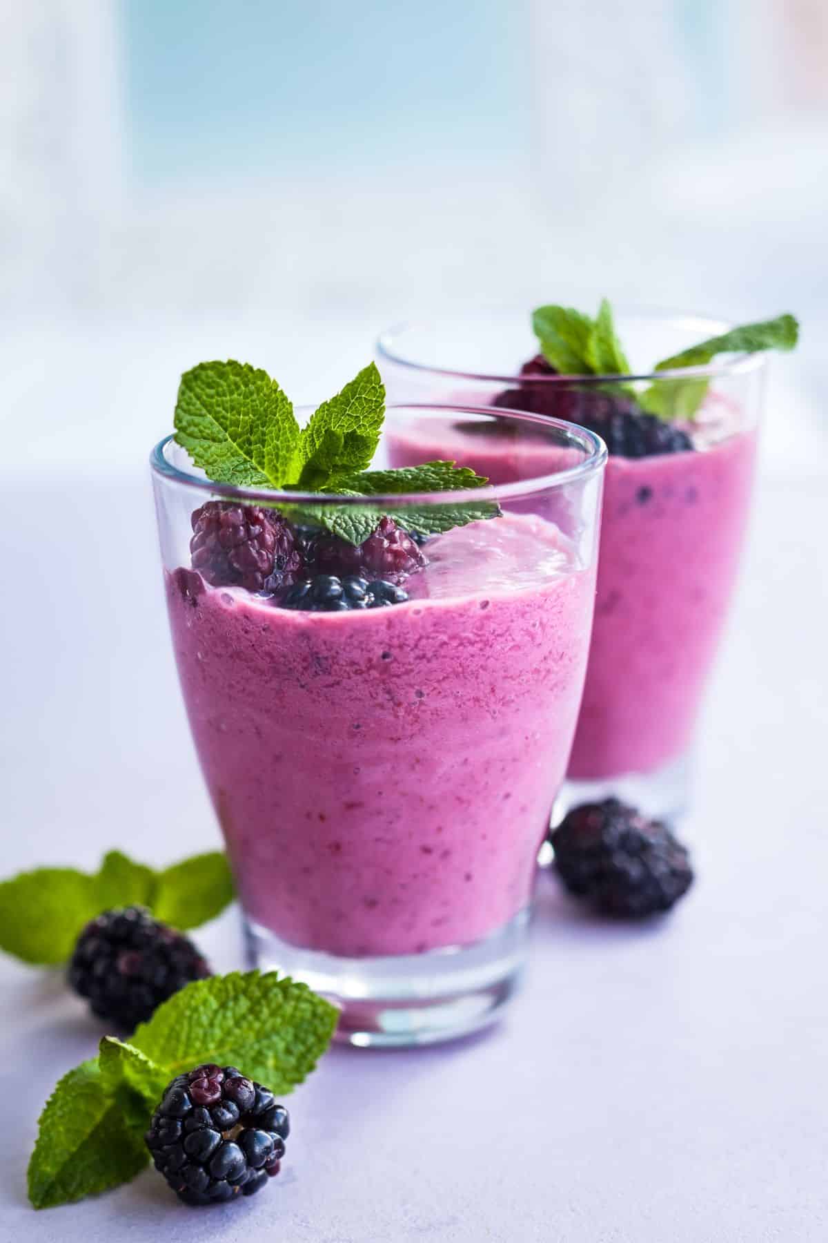 Two short glasses of blackberry smoothie topped with fresh mint leaves.