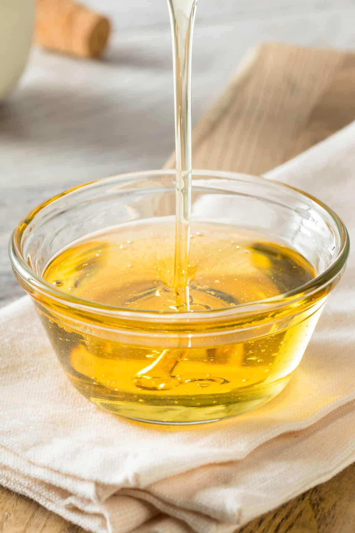 Agave nectar pouring into clear bowl on napkin and cutting board.