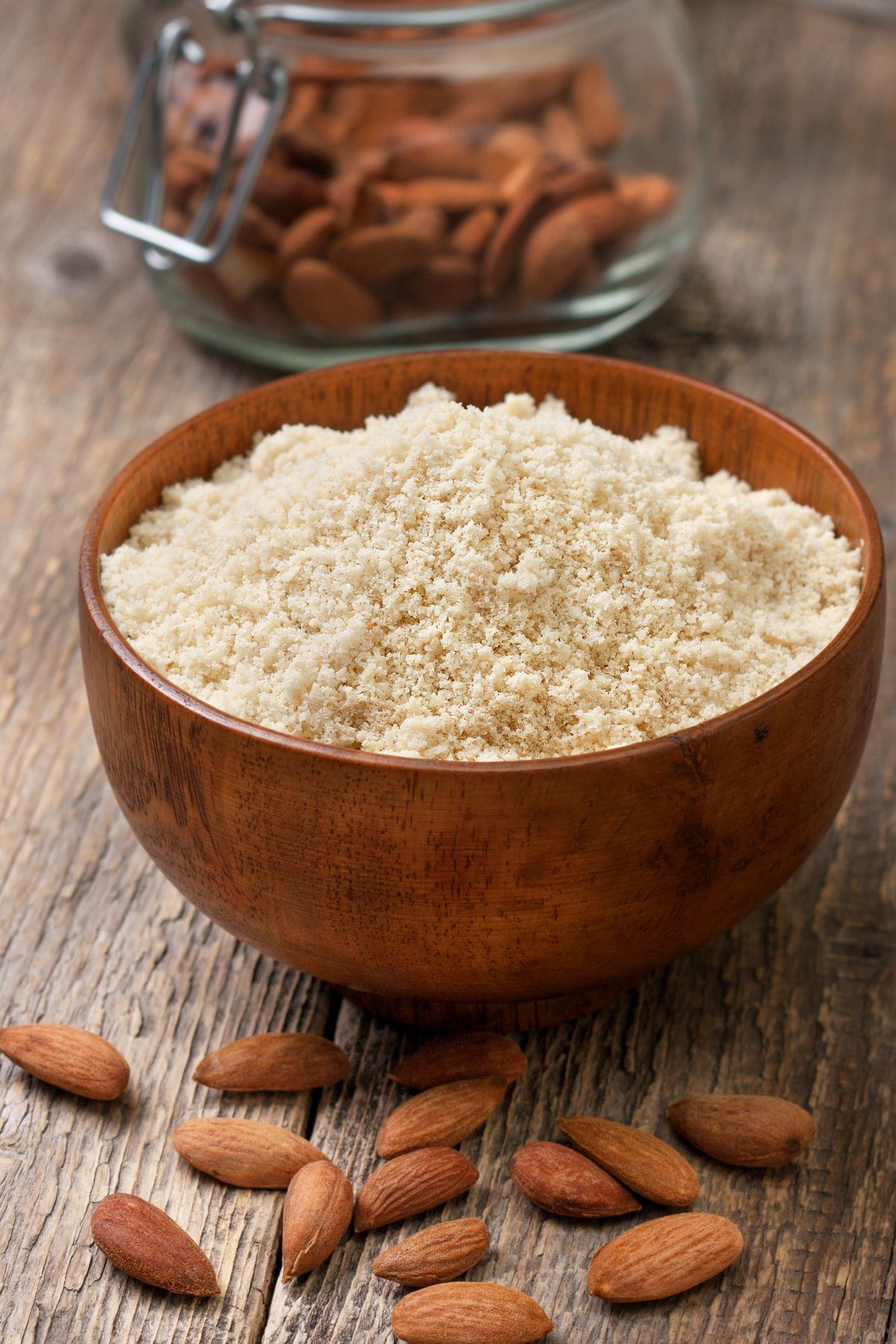 Bowl of almond flour with whole almonds on wooden surface.