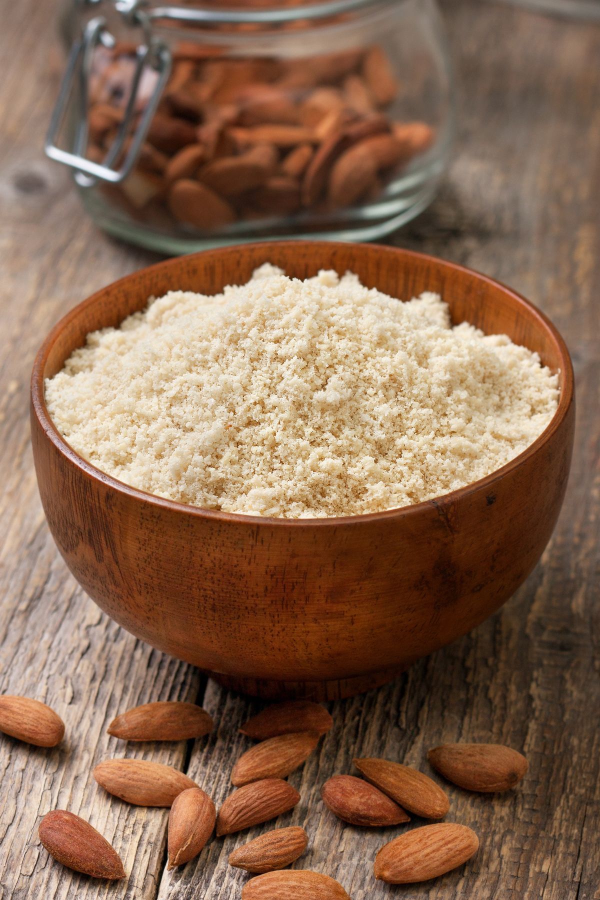 Bowl of almond flour with raw almonds on wooden surface.