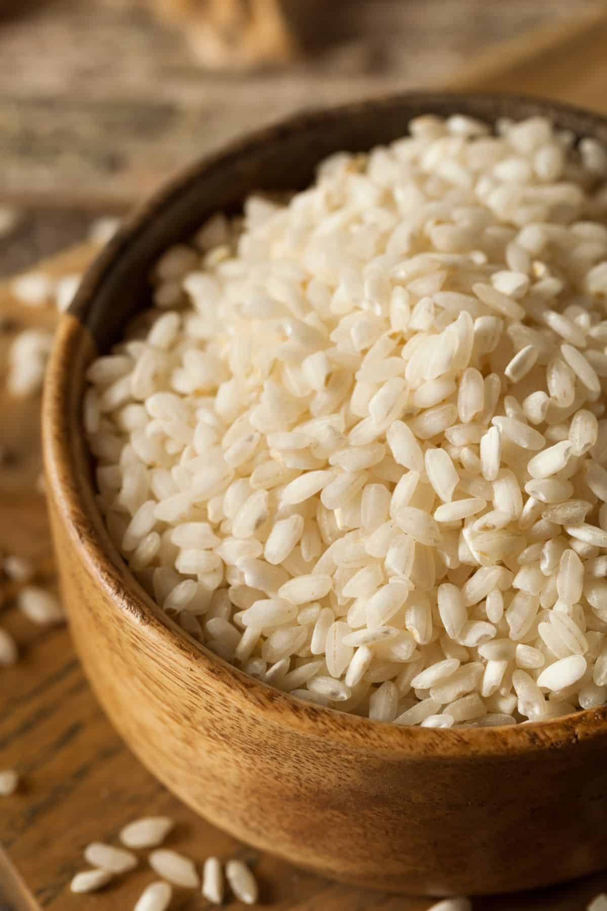 Bowl of arborio rice on wooden surface.