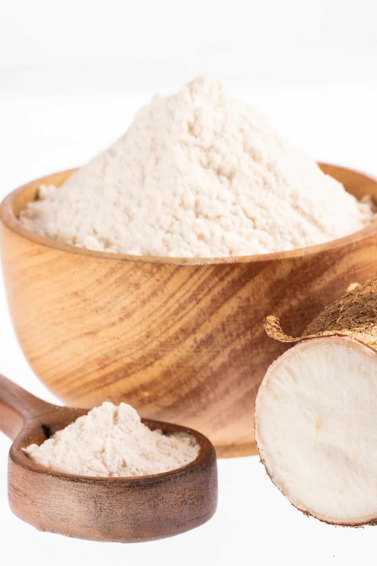 Bowl and spoonful of arrowroot flour on white background.
