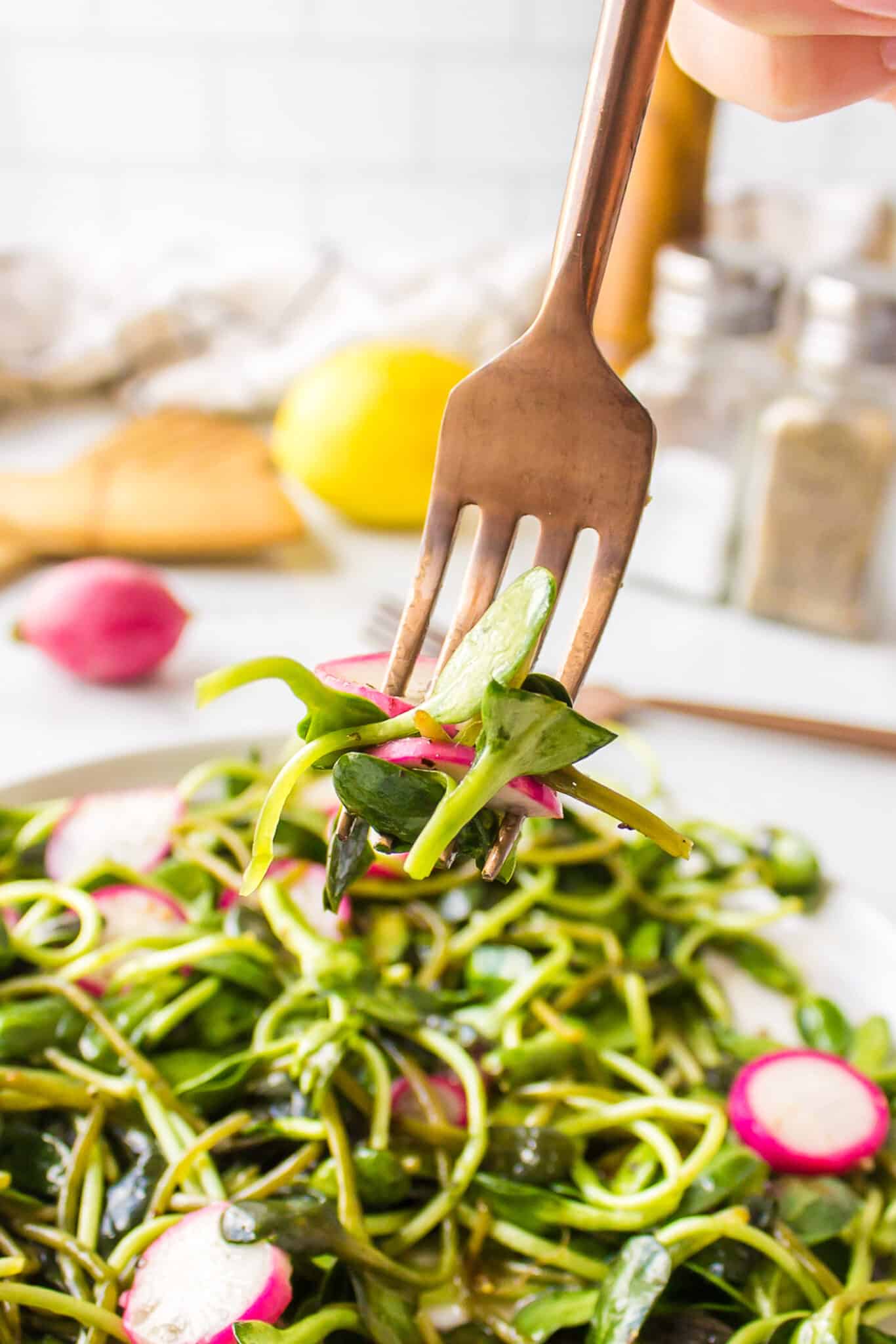 A fork lifting up a bite of micro greens salad from a plate.