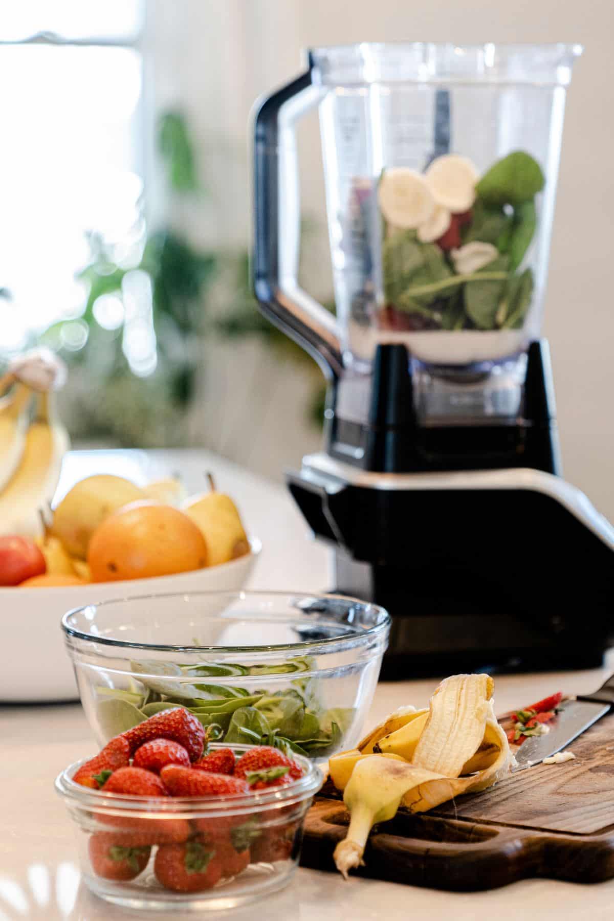 Bowl of fruit and smoothie ingredients next to a blender on the counter.