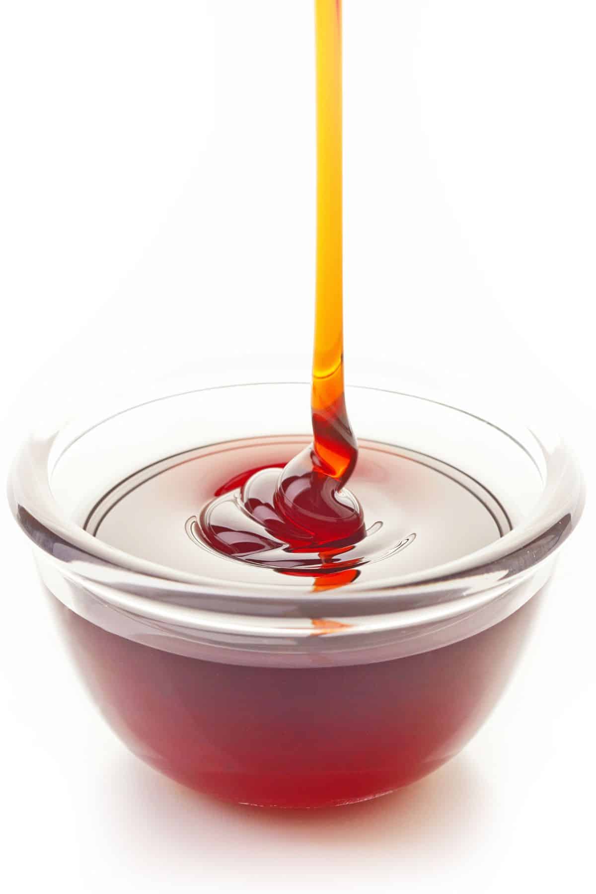 Brown rice syrup pouring into clear bowl on white background.