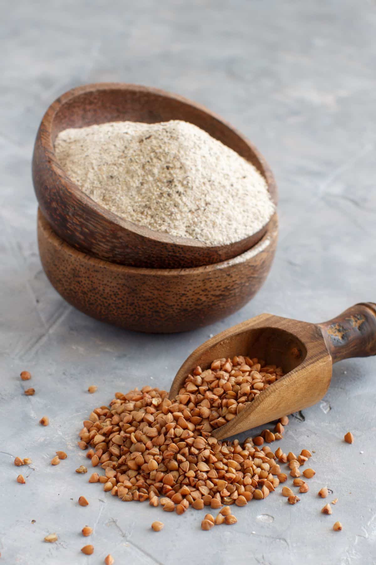 Bowls of buckwheat flour and scoop of buckwheat kernels.