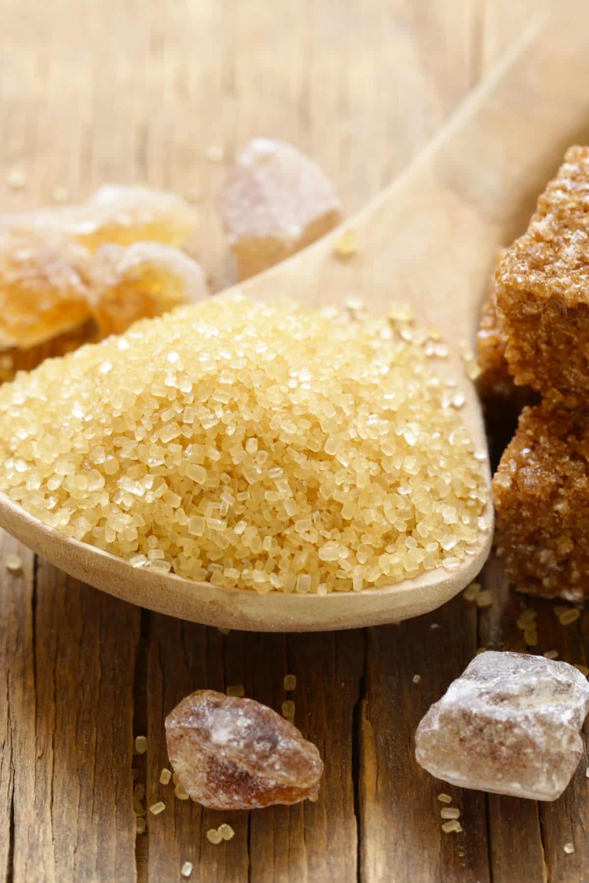 Spoonful of cane sugar with blocks of sugar on wooden surface.