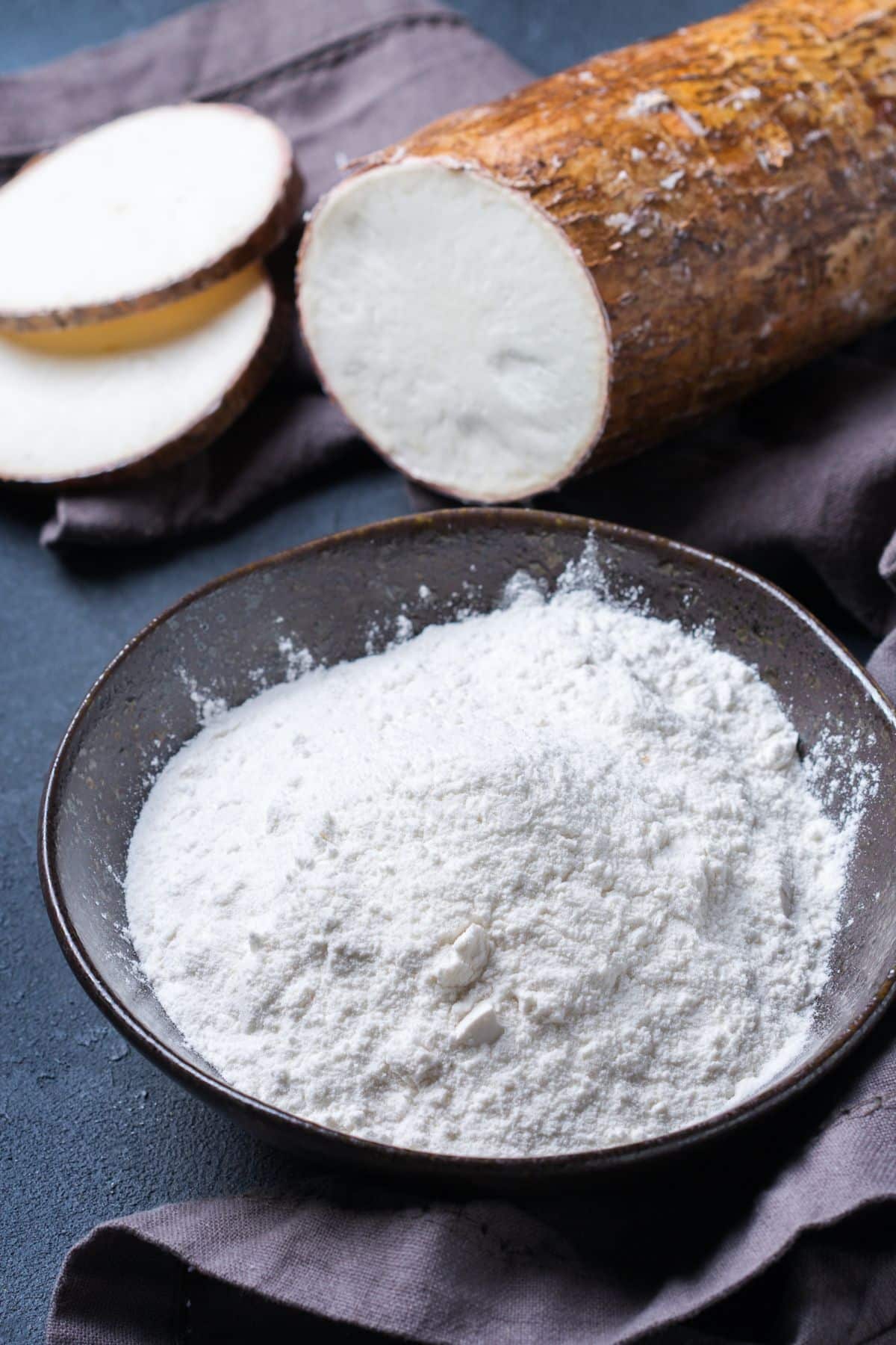 Bowl of cassava flour on table with cassava root.