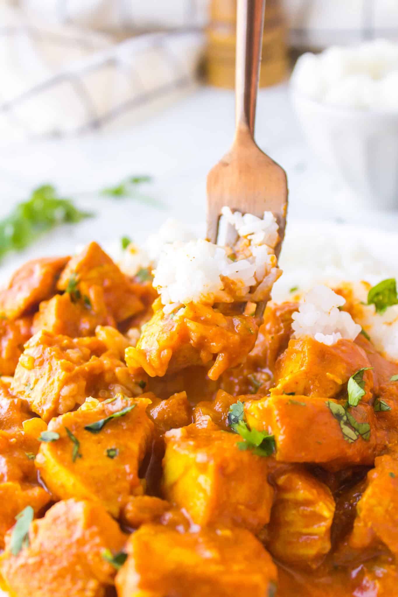 A fork lifting up a bite of chicken curry with white rice.