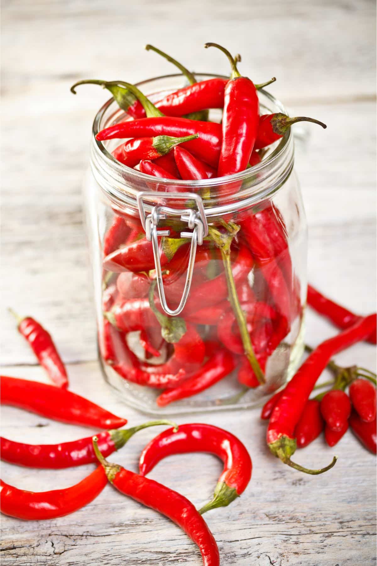 Jar of chili peppers on wooden surface.