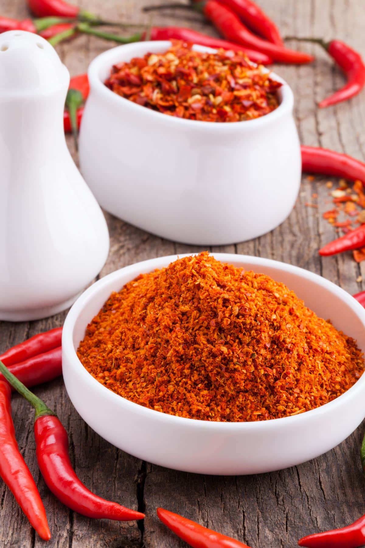 Bowl of chili powder with fresh chilis on wooden surface.