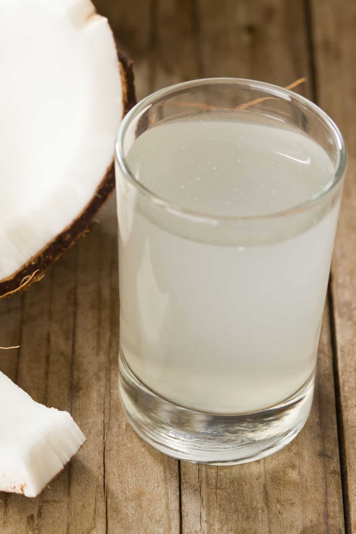 A glass of coconut water next to a fresh coconut on a wooden table.