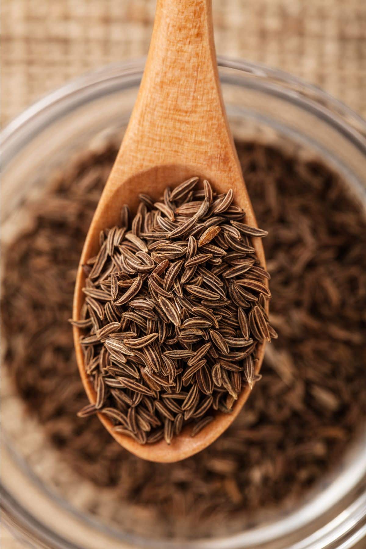 Scoopful of cumin seeds over bowl of caraway.