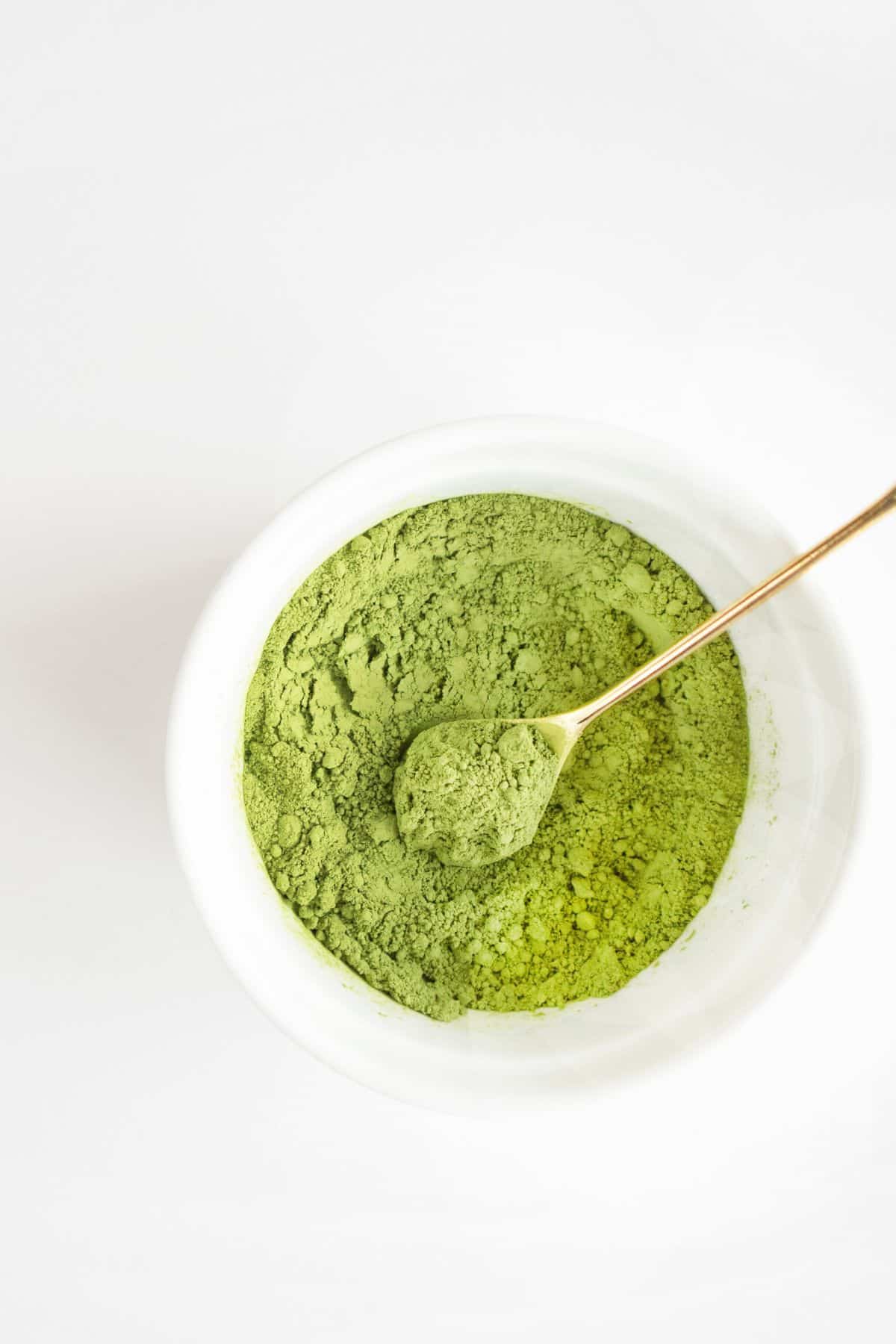 A small white bowl of green matcha powder with a gold spoon.