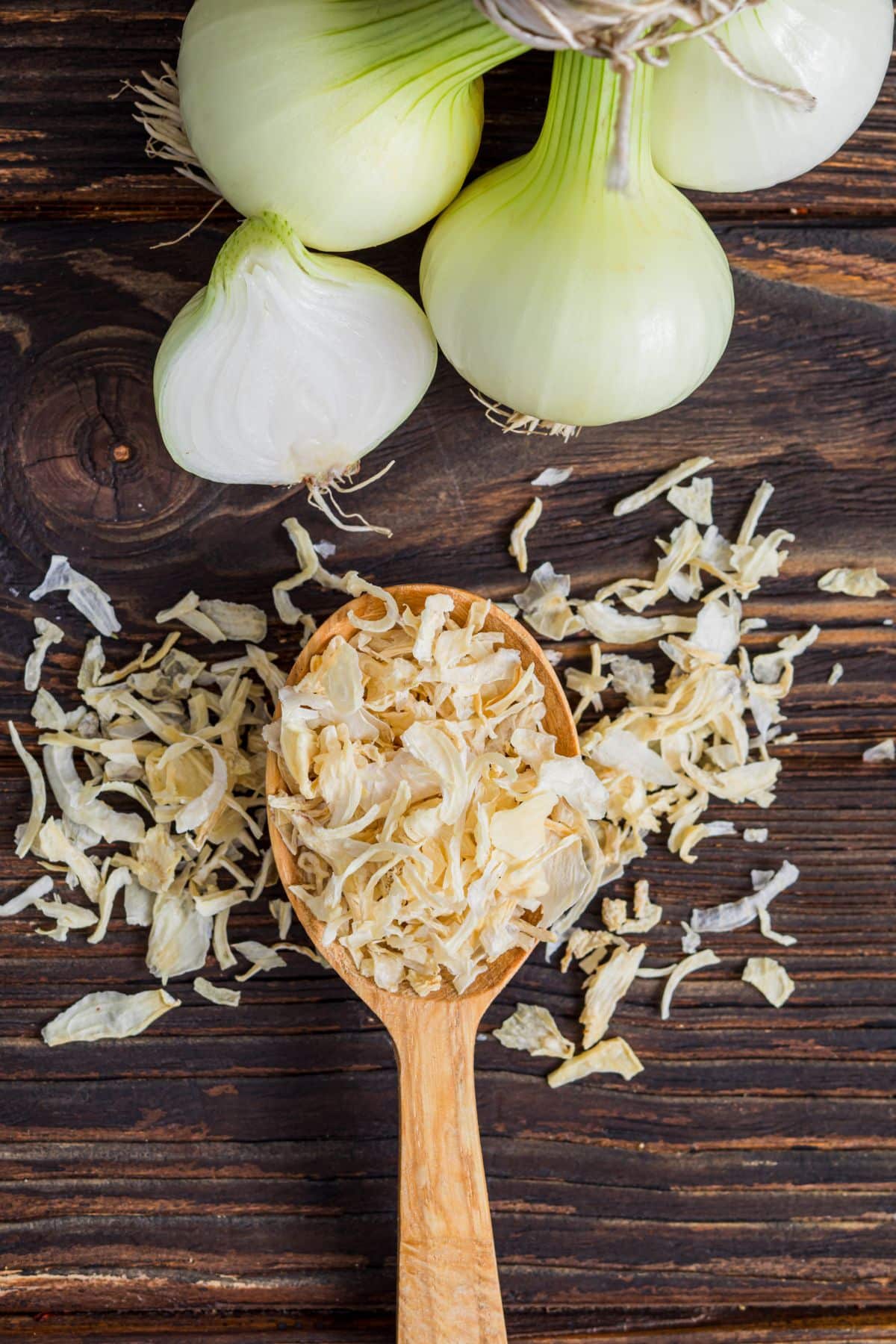 Wooden spoon with dried onion flakes on wooden surface.