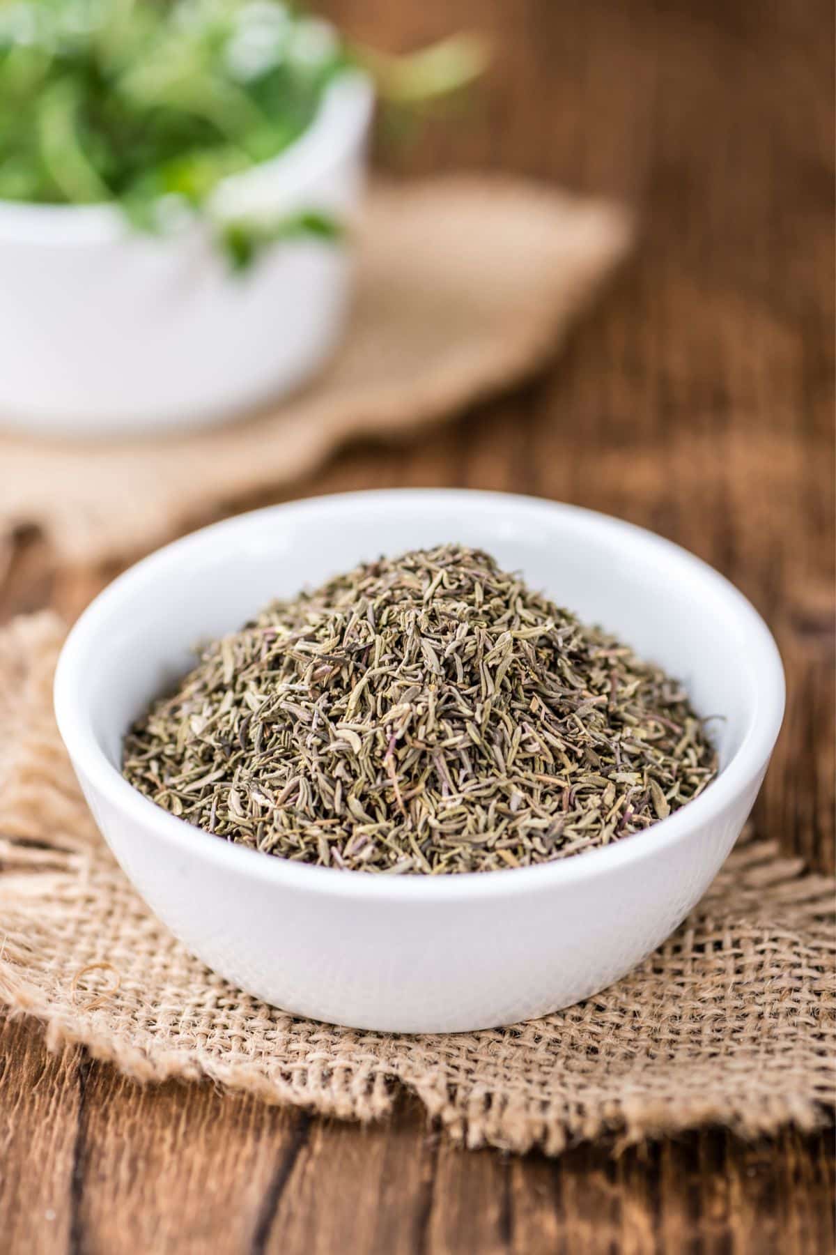 Bowl of dried thyme on burlap on wooden surface.