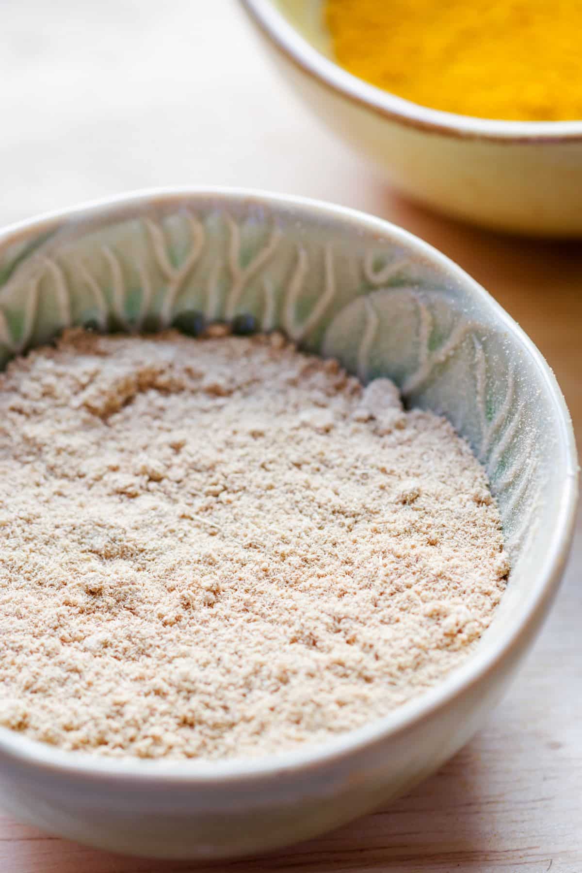 Bowl of galangal powder on wooden surface.