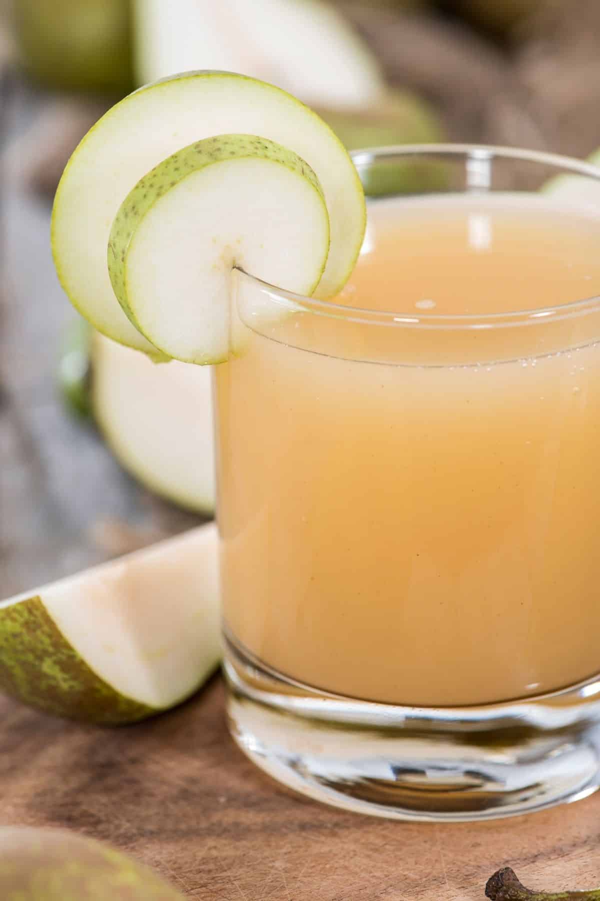 glass of pear juice with a slice of pear on rim.