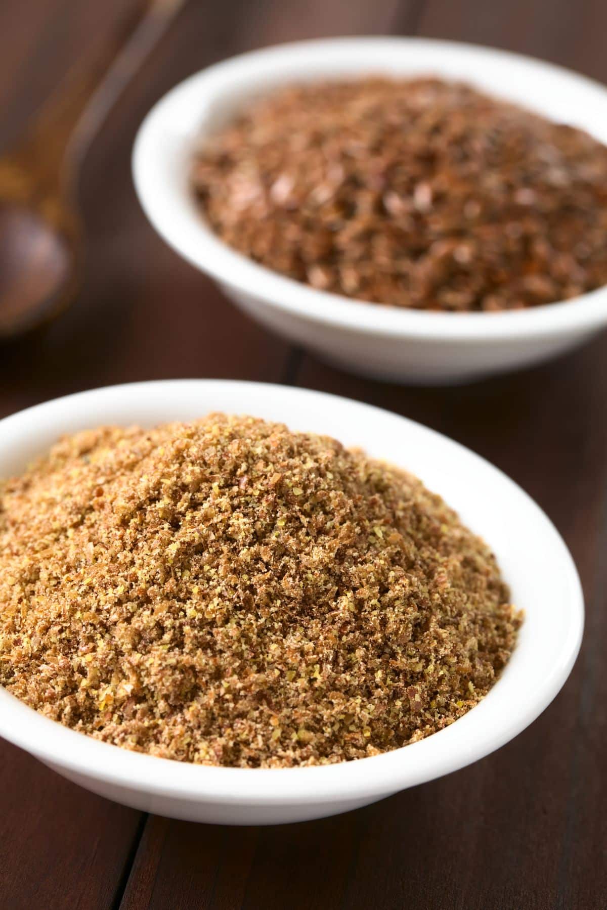 Bowl of ground flax on wooden surface.