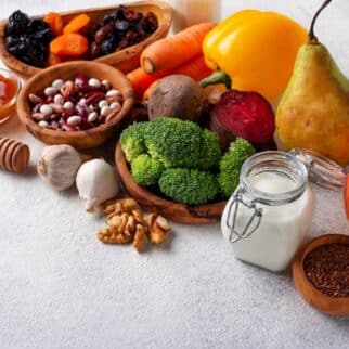 Fresh produce, dried beans, and honey on a white surface.