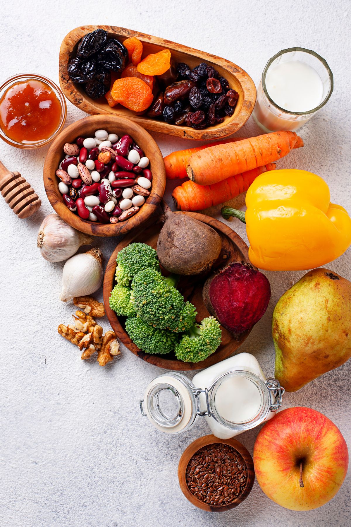 Fresh produce, dried beans, and honey on a white surface.