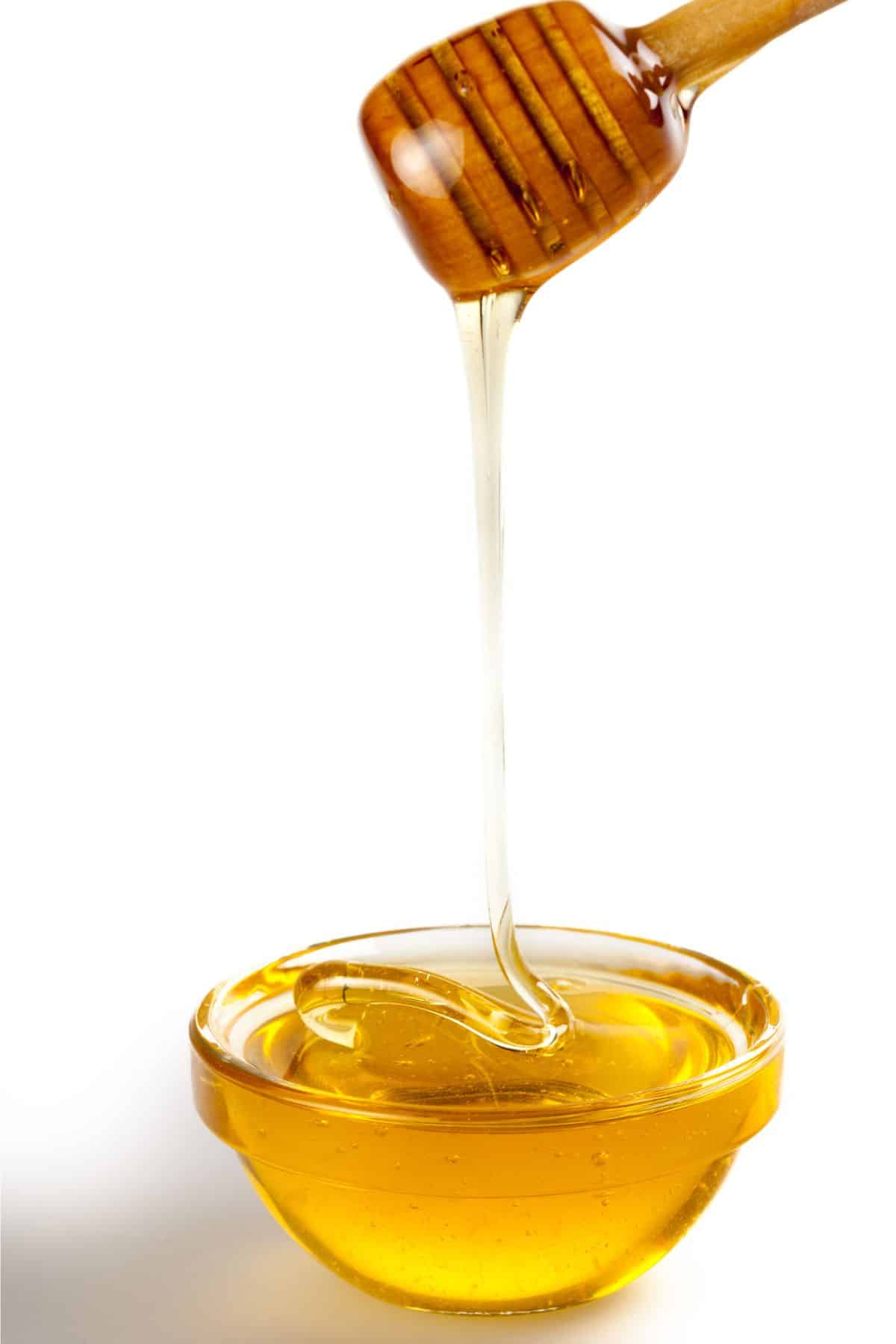 Honey pouring into clear bowl on white background.
