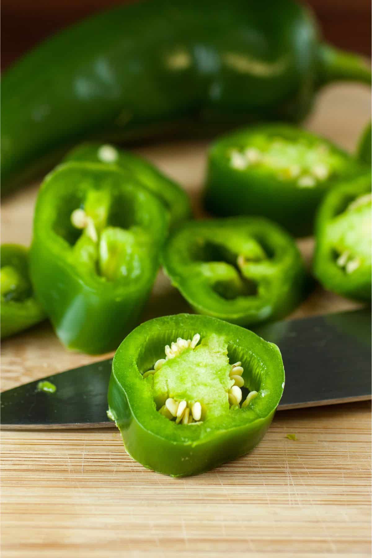 Sliced and whole jalapenos on wooden surface.