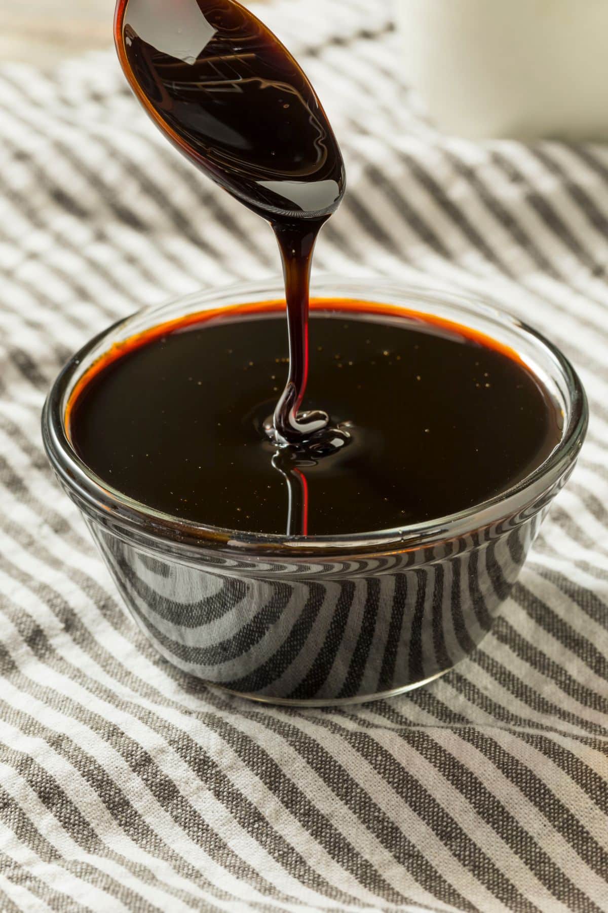 Molasses pouring into clear bowl on patterned kitchen towel.