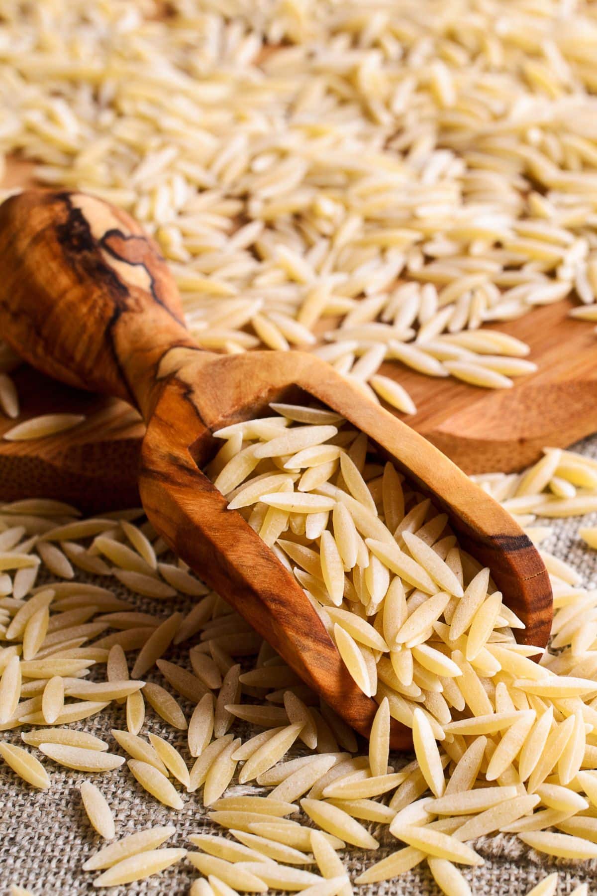 Scoop of orzo pasta on cutting board and burlap. 