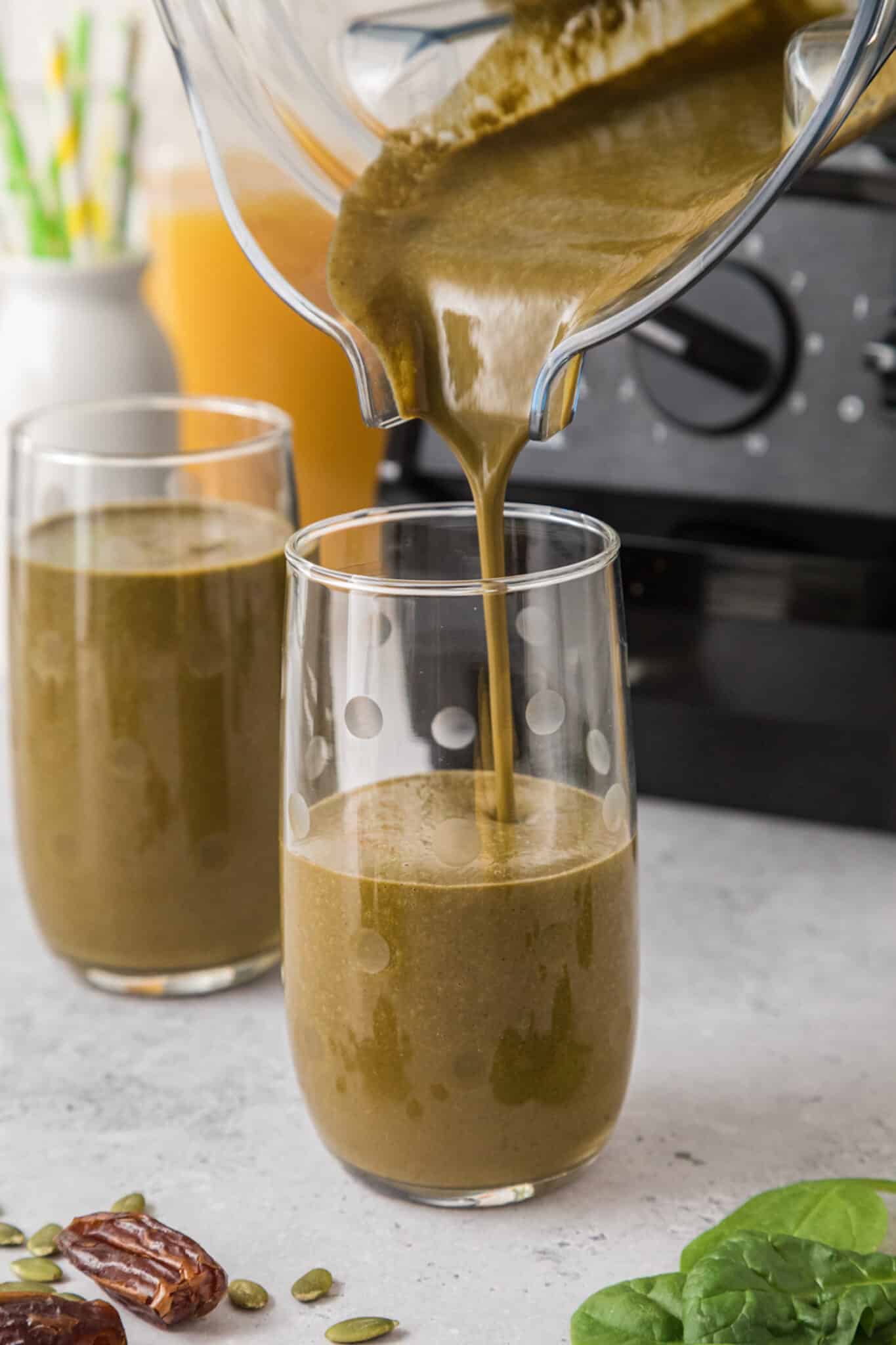 A blender jar pouring a green smoothie into a tall glass.