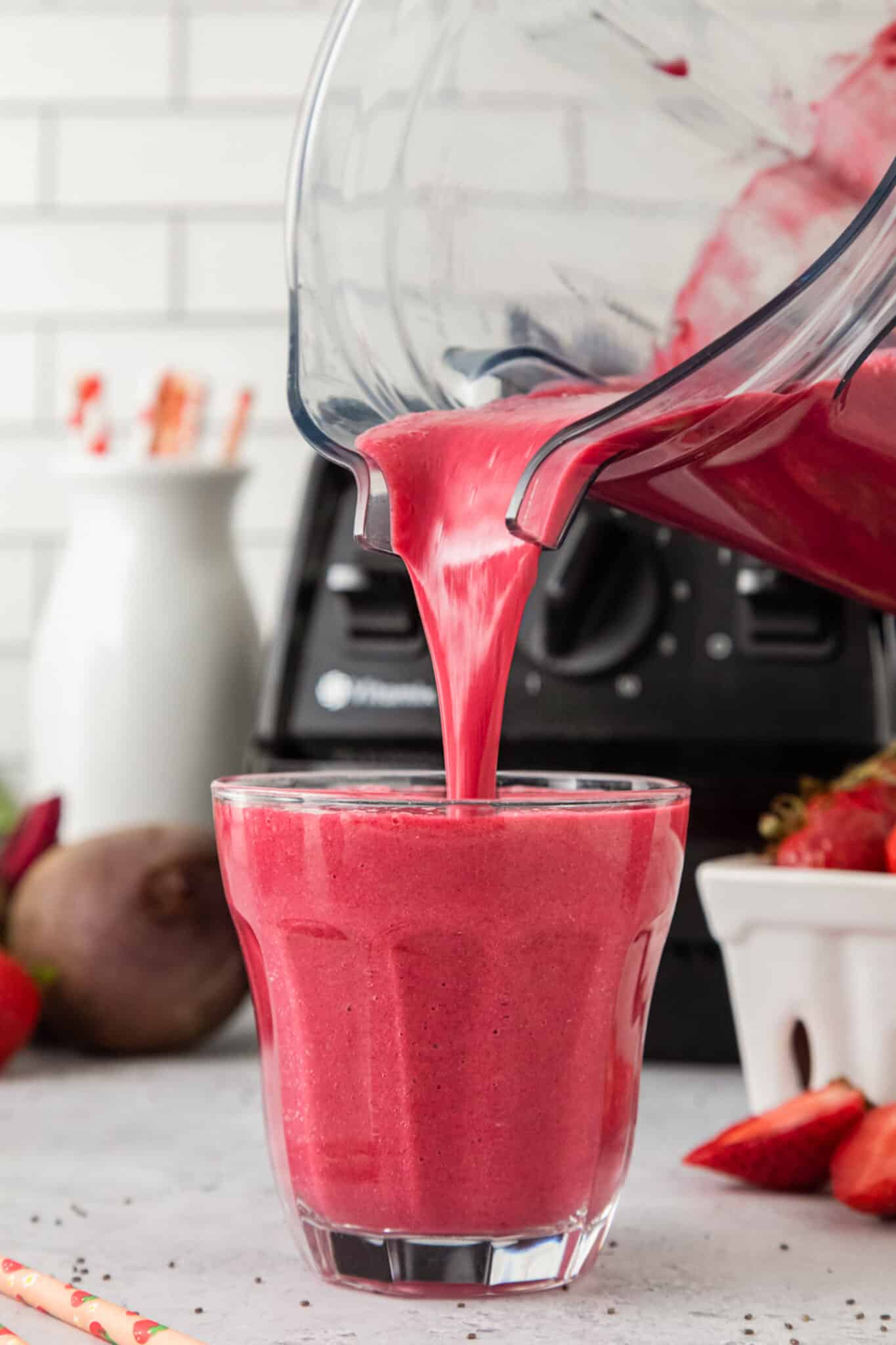 A strawberry smoothie being poured from a blender jar into a glass.