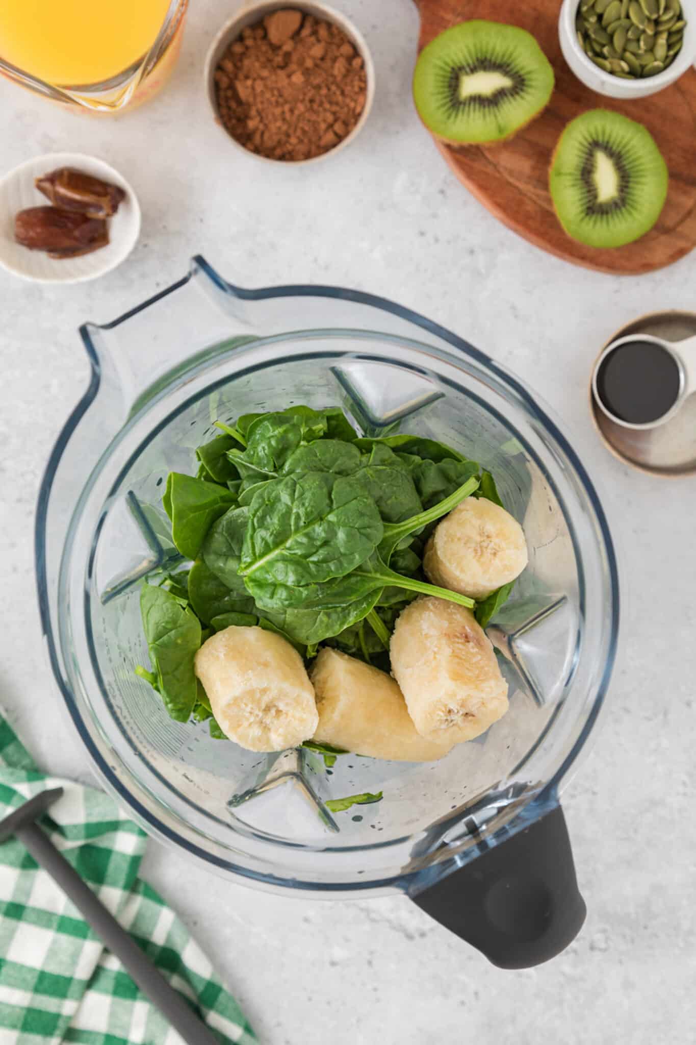 Top view of a blender jar with spinach and frozen bananas.