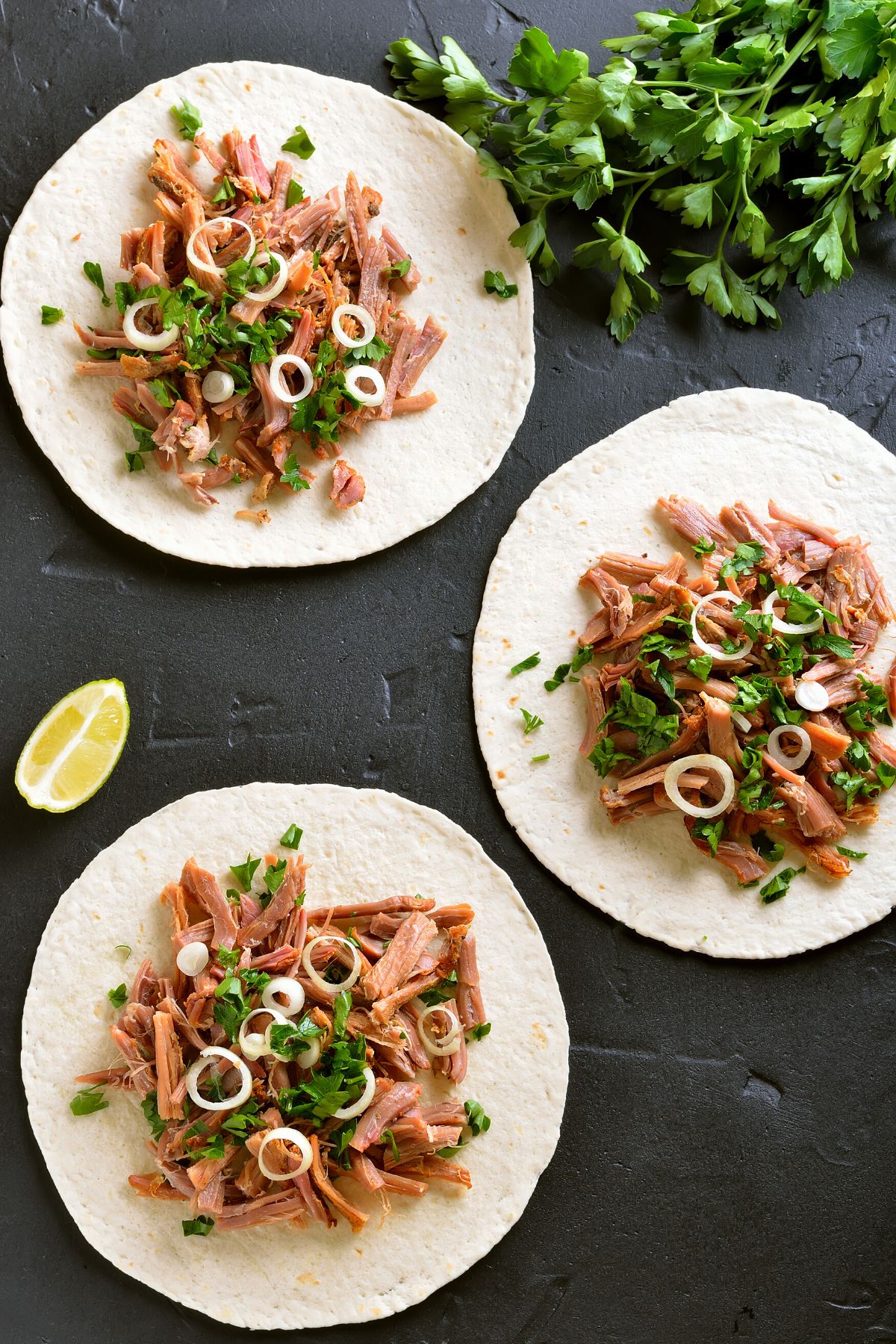 Pulled pork on small flour tortillas on a black surface.